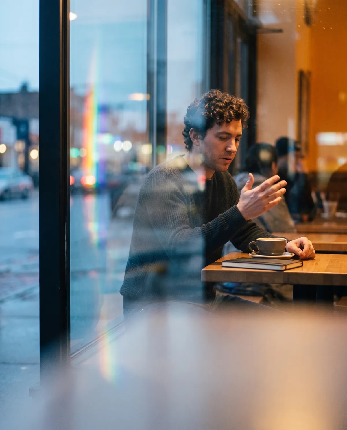 A man at a café window seat talking an idea through over coffee.